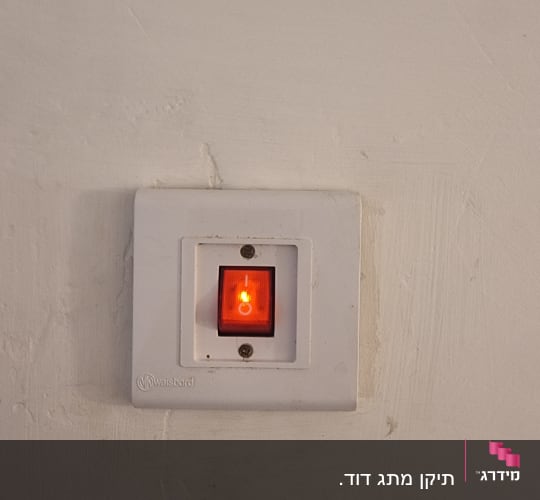 מתג חשמלי עם אור אדום דולק על קיר
